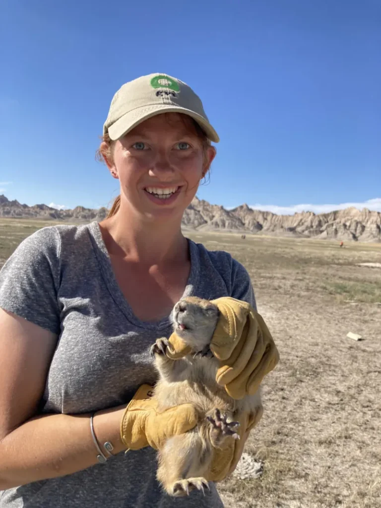 a picture of a woman wearing grey shirt and a hat holding a wild animal